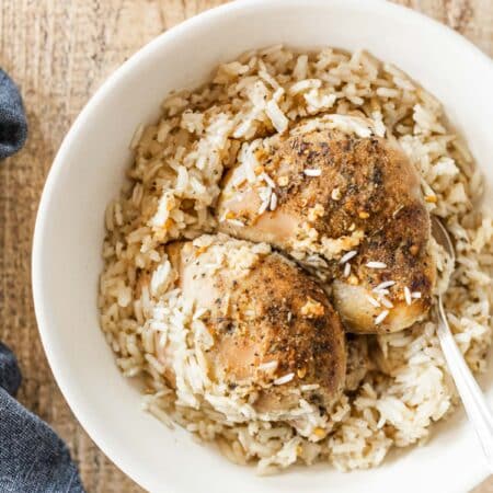 Two cooked chicken thighs with rice in a bowl.