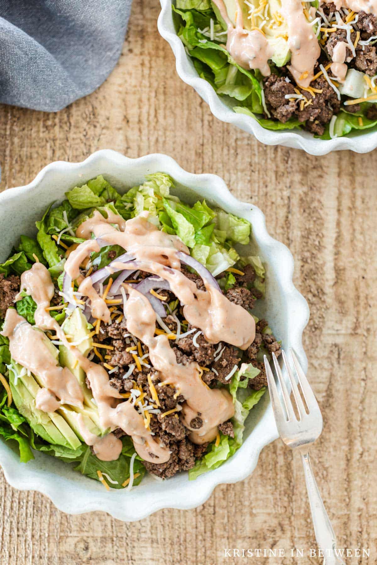 A hamburger bowl with dressing on top and a fork leaning up on the bowl.