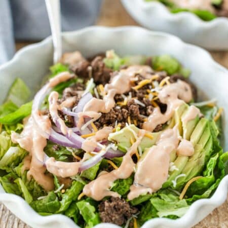 A hamburger bowl with dressing on top and a fork leaning up next to it.