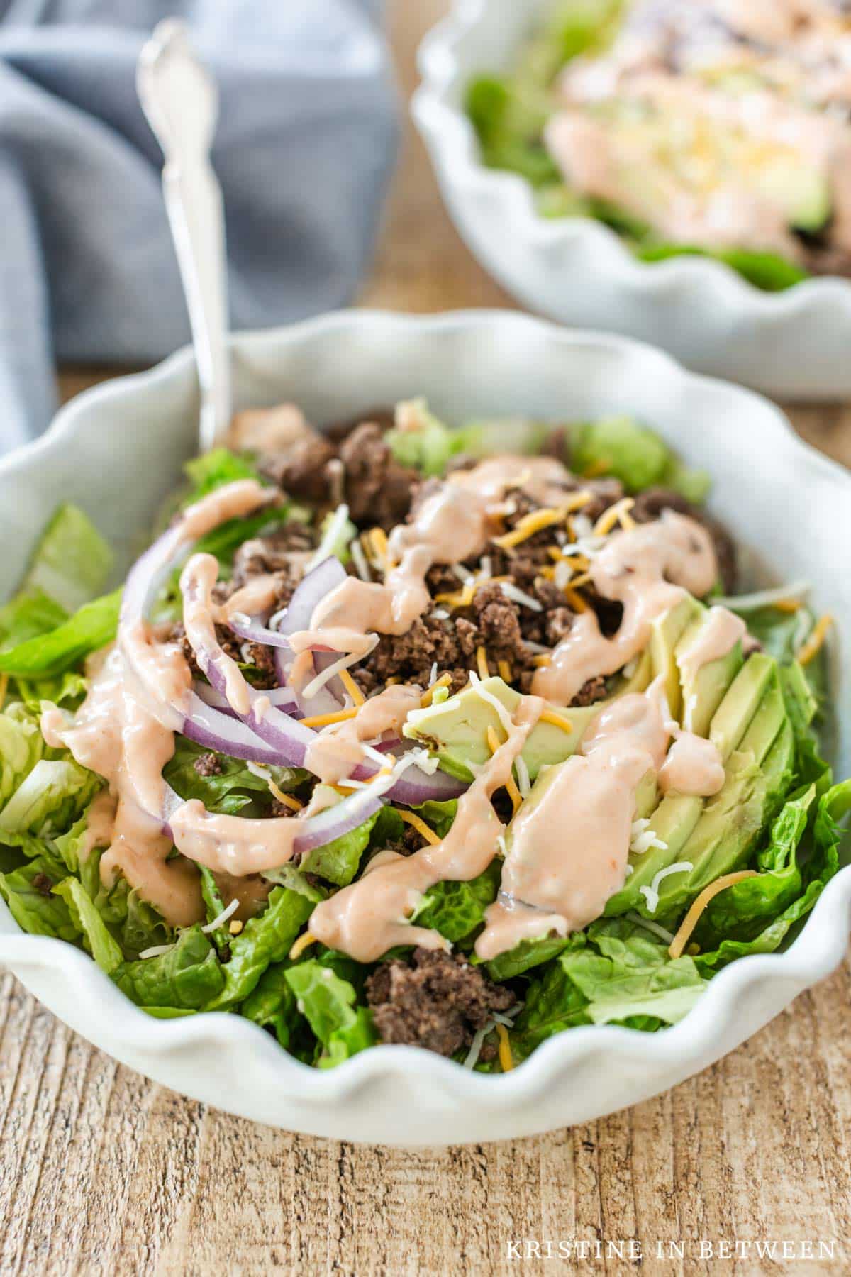 A hamburger bowl with dressing on top and a fork leaning up next to it.