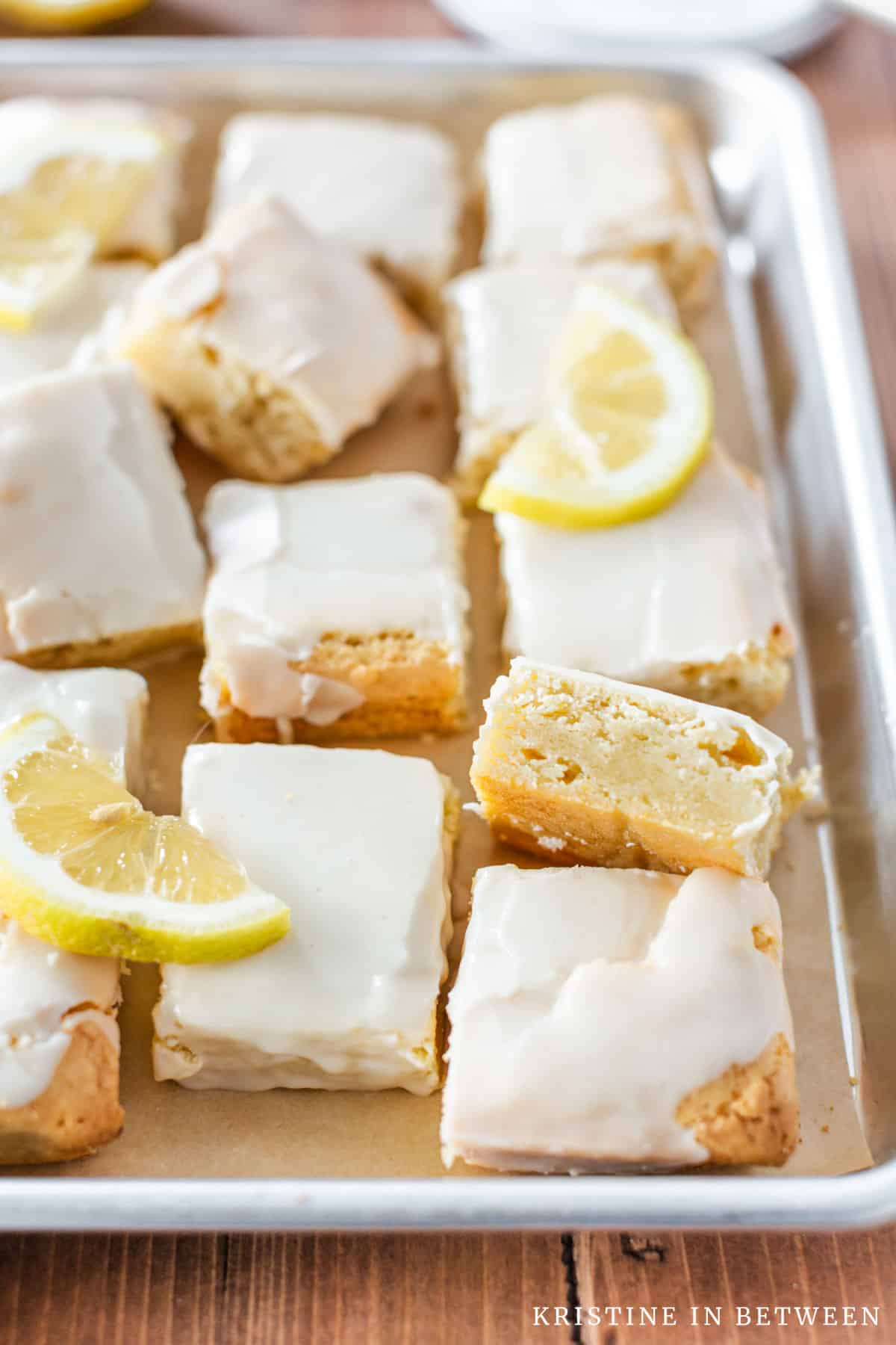 Lemon brownies sitting on a cookie sheet with sliced lemons on top.