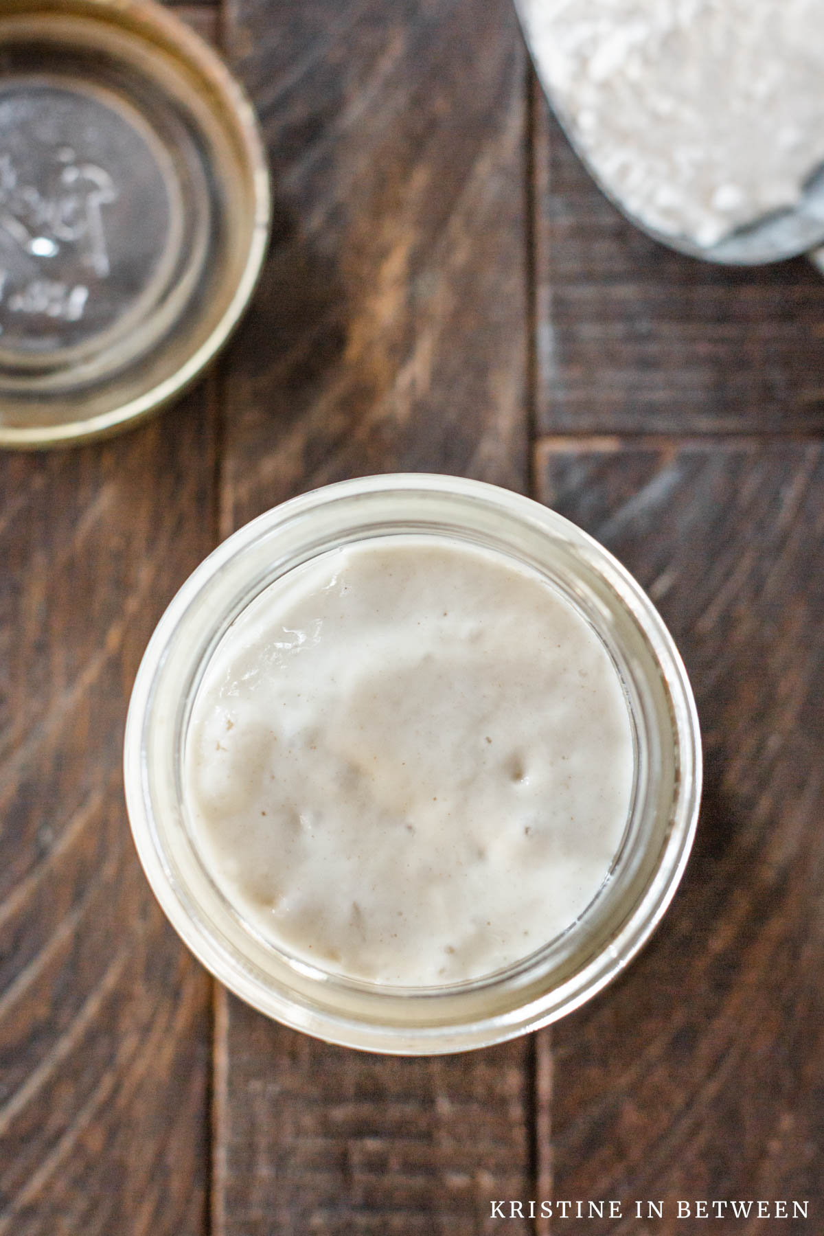 A jar of sourdough starter with a scoop of flour sitting next to it.