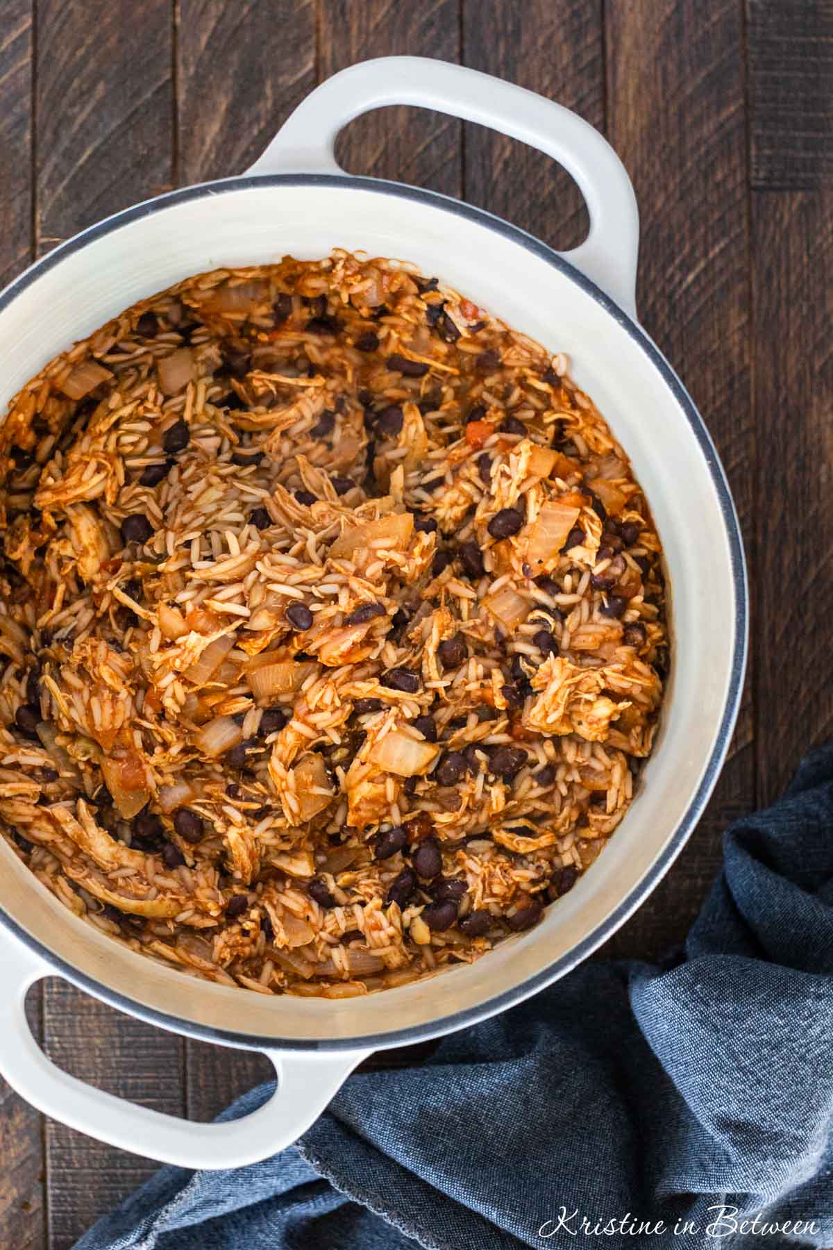 A white dutch oven with cooked chicken taco rice casserole with a blue napkin sitting next to it.