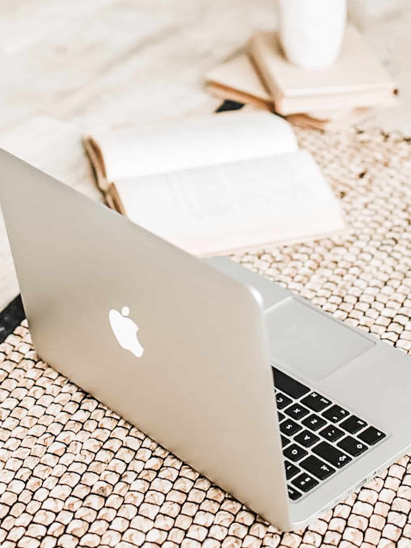 A laptop sitting on the floor with an open book next to it.