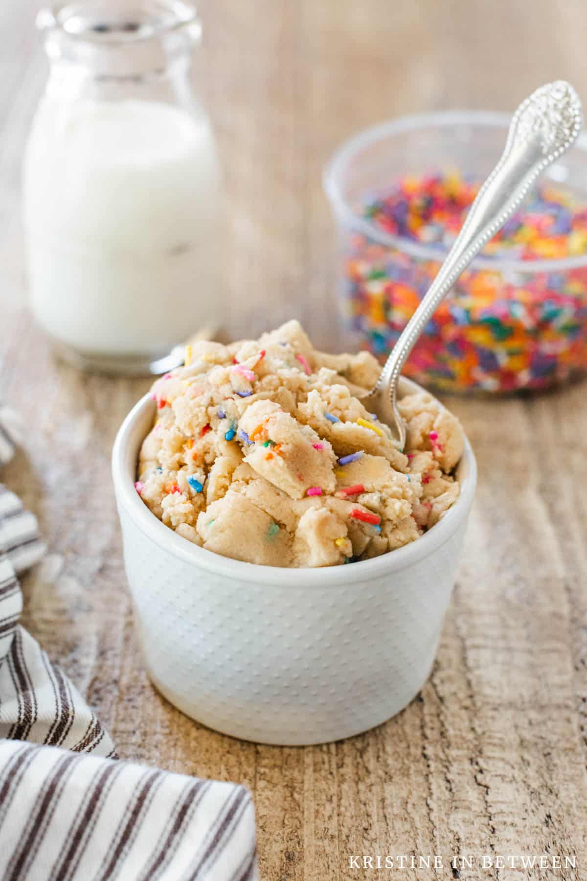 A small bowl of sugar cookie dough with a spoon in it and a jar of milk in the background.