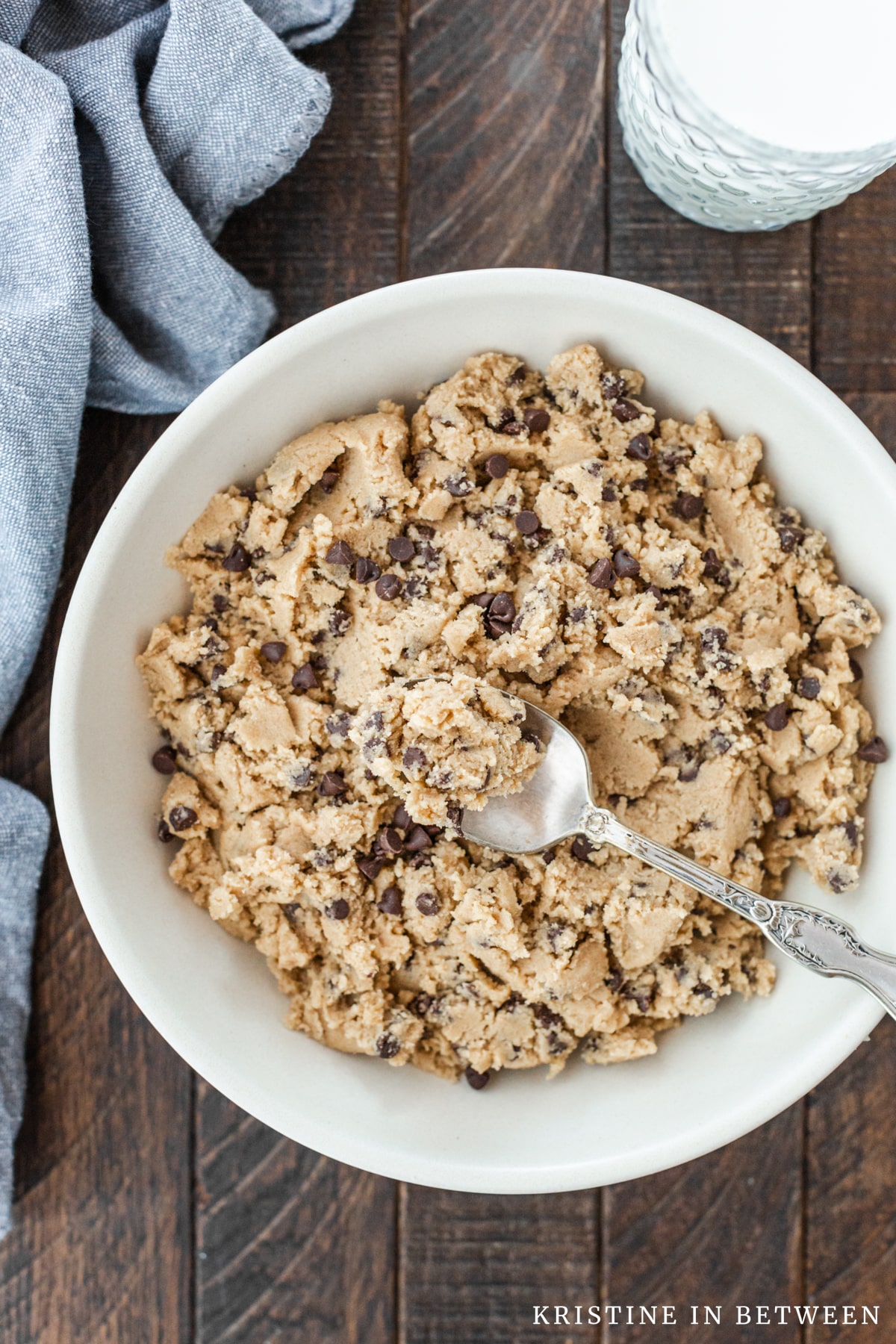 A spoonful of cookie dough sitting on top of a bowl of cookie dough with a glass of milk in the background.