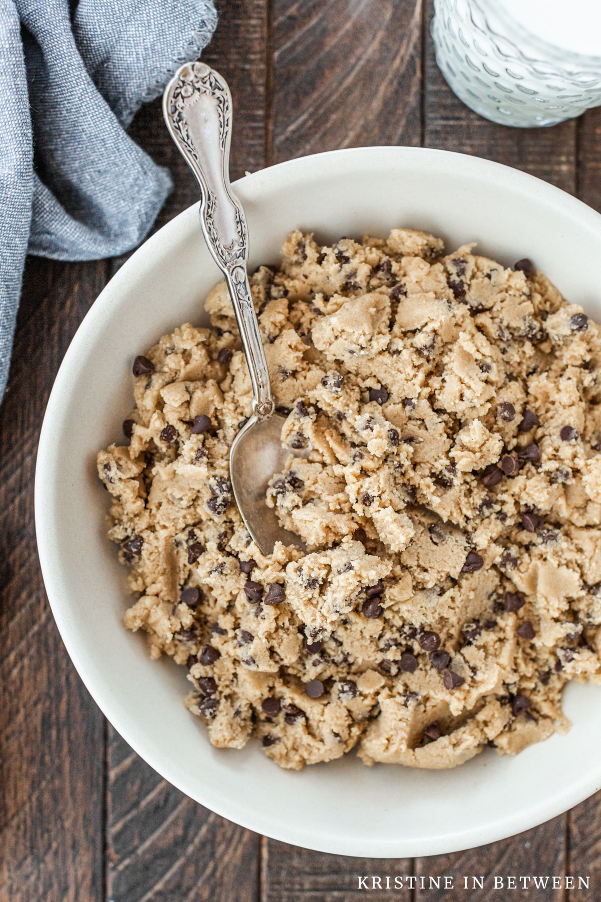 A bowl of chocolate chip edible cookie dough with a spoon in it.
