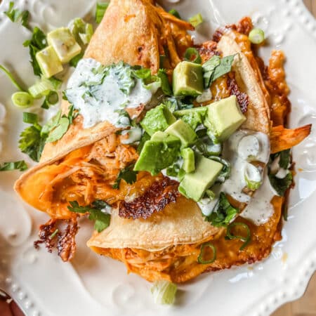 Two tacos sitting on a white plate with chopped avocado and cilantro on top.