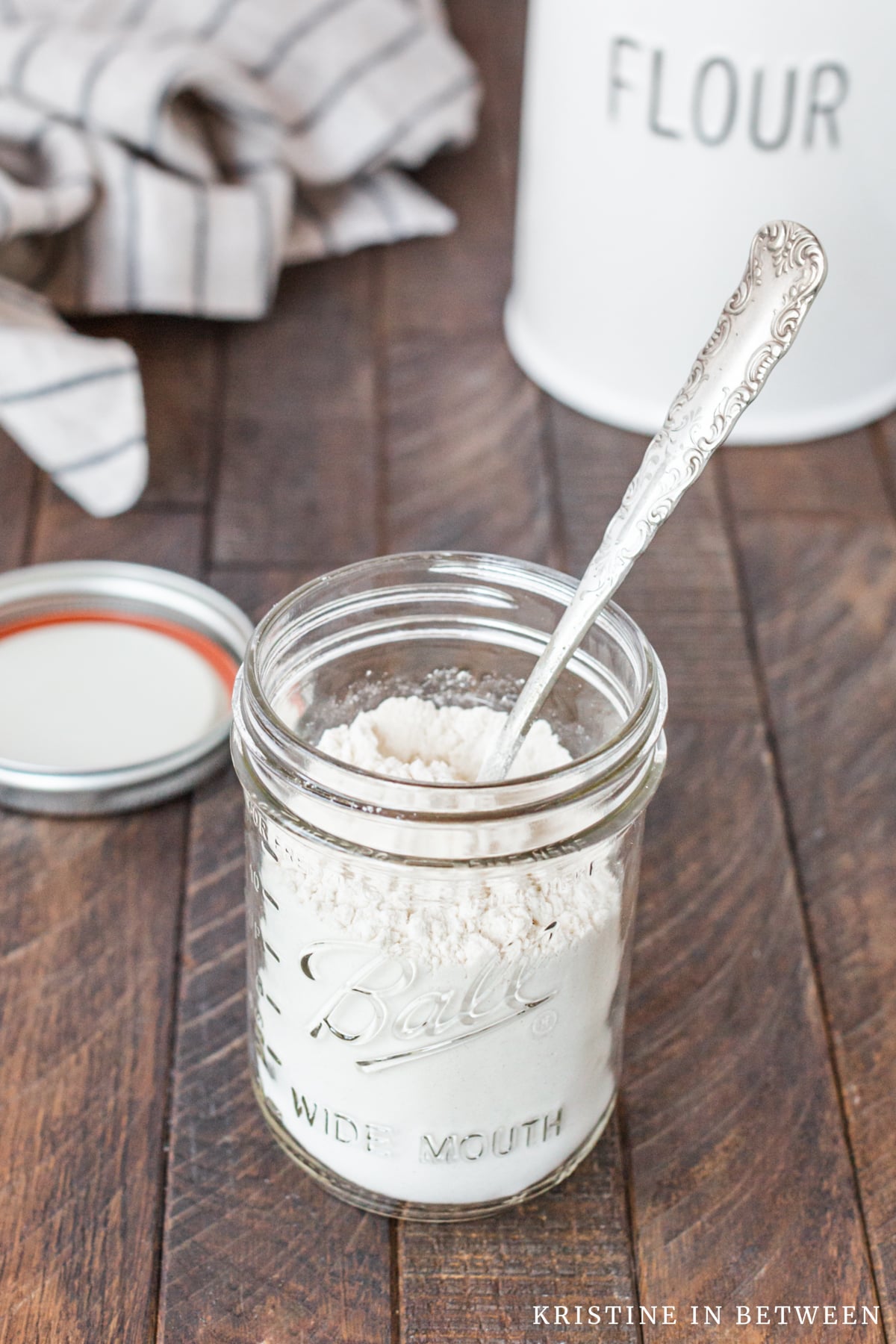 A mason jar with heat treated flour and a canister of flour in the background.