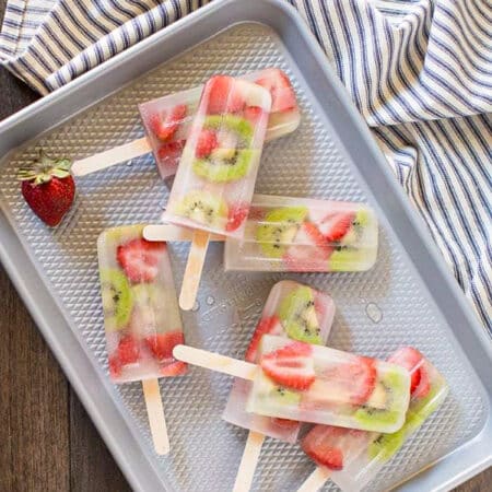 Strawberry kiwi popsicles laying on a cookie sheet with a blue striped napkin next to them.
