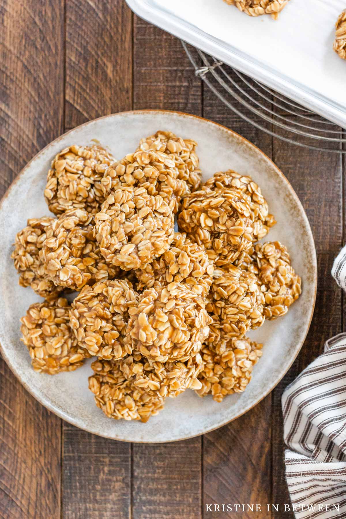 Cookie butter no-bake cookies piled up on a white plate with more cookies on a tray in the background.