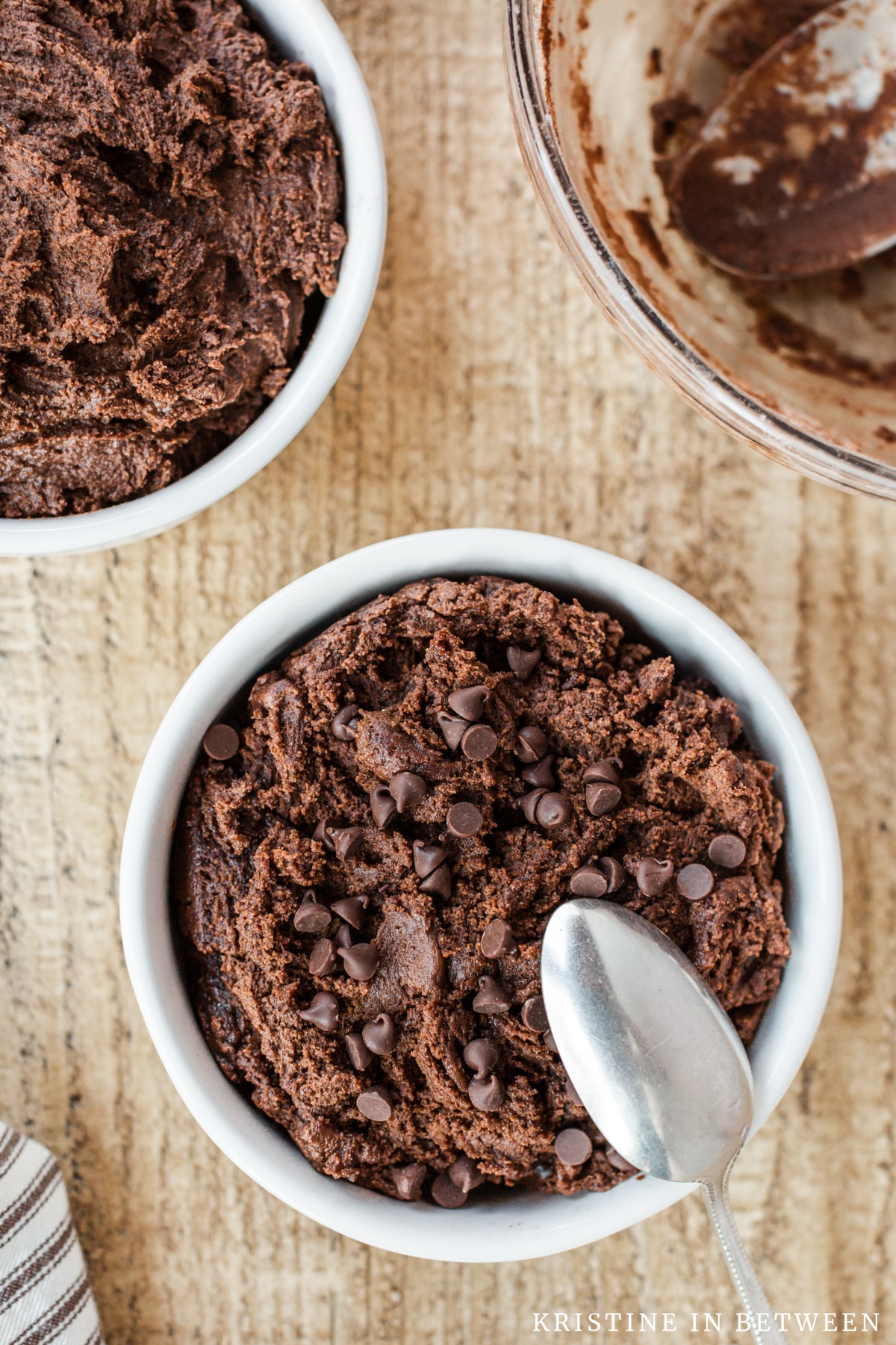 Edible chocolate cookie dough with chocolate chips on top sitting in white bowls with spoons.
