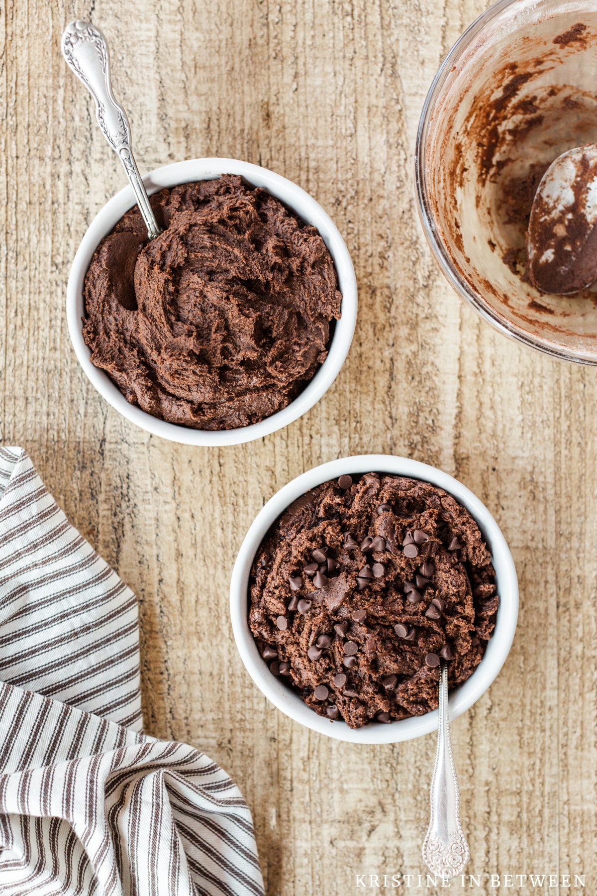Two bowls of edible cookie dough in white bowls with antique spoons sitting on a wooden board.