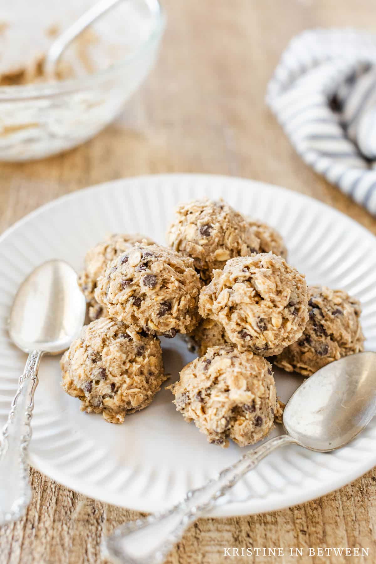 Edible oatmeal cookie dough scooped onto a white plate with two spoons.