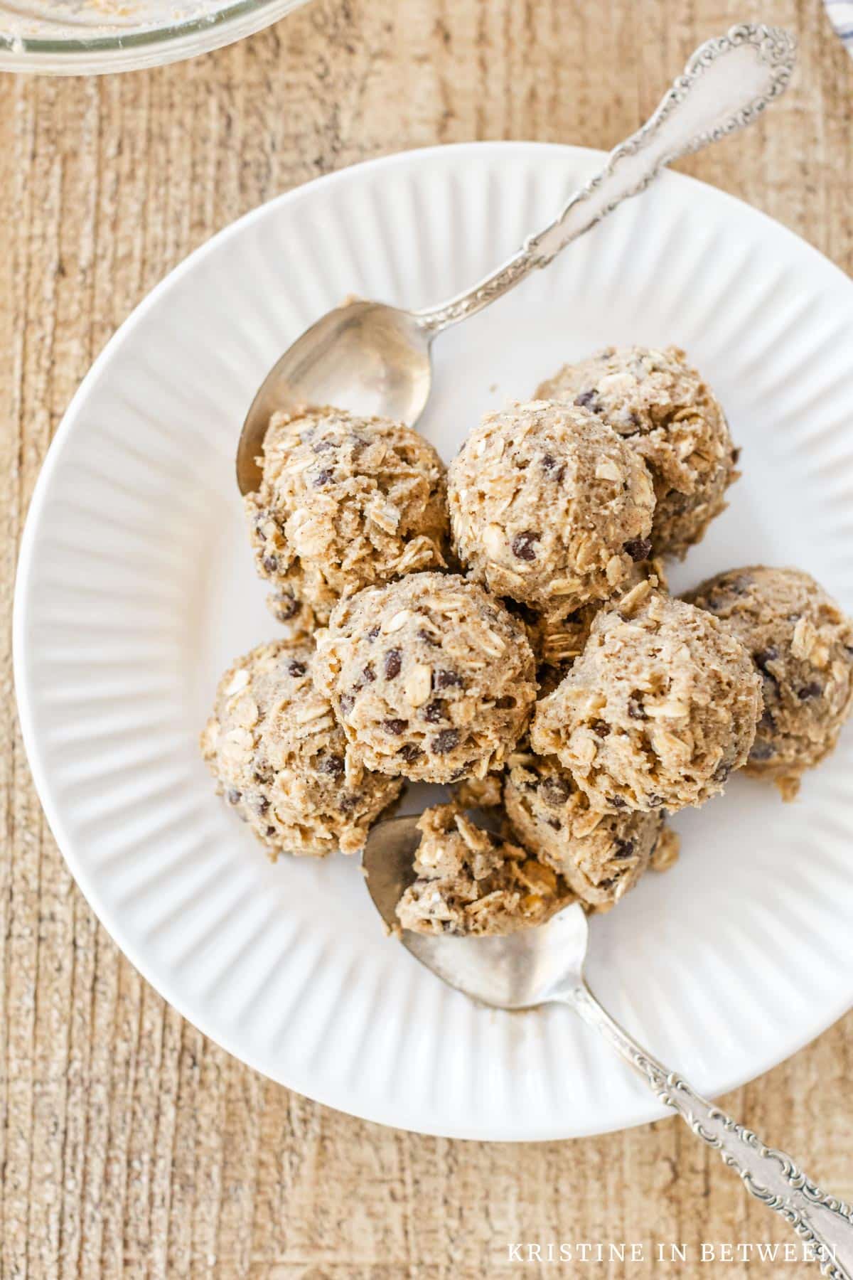 Edible oatmeal cookie dough with chocolate chips scooped onto a white plate with two spoons.