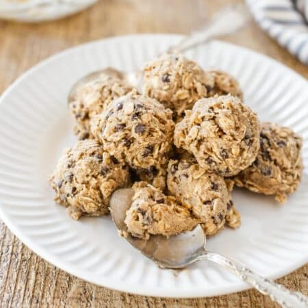 Edible oatmeal cookie dough scooped onto a white plate with two spoons.