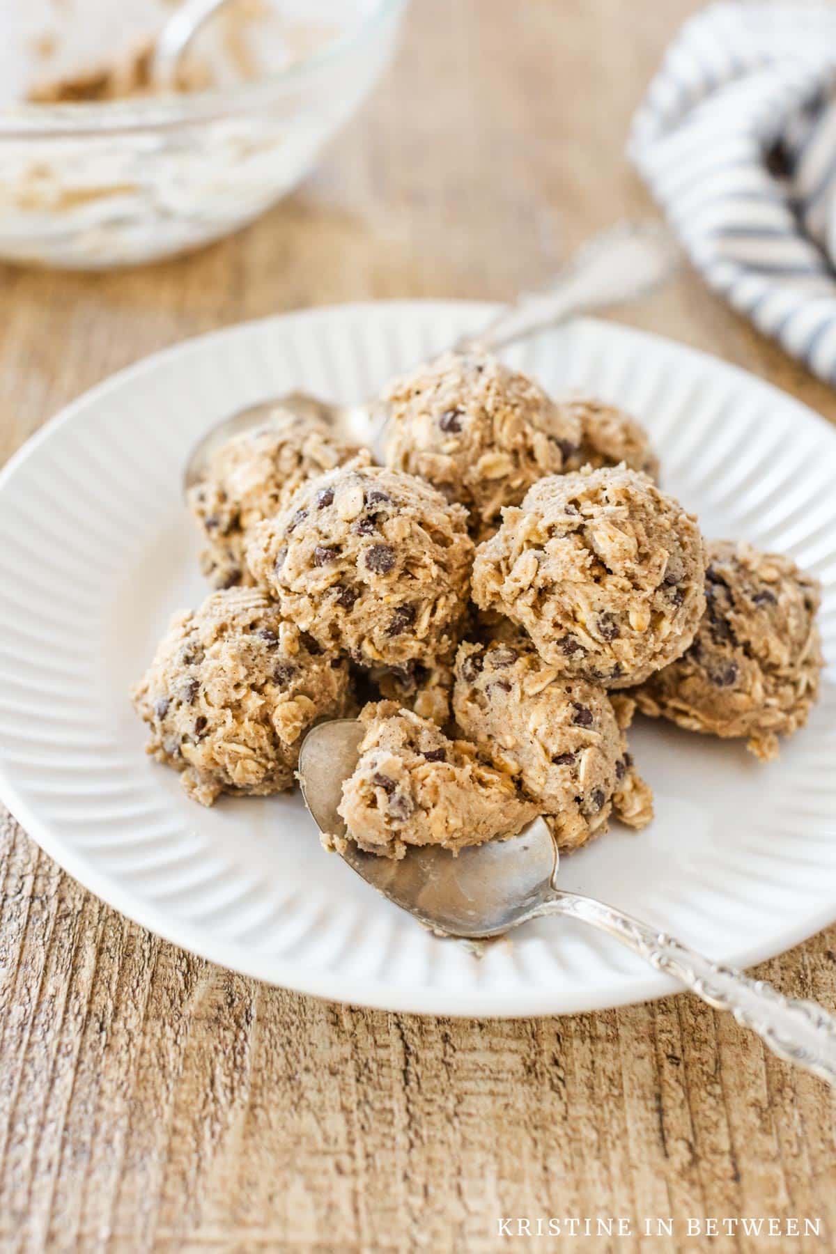 Edible oatmeal cookie dough scooped onto a white plate with two spoons.