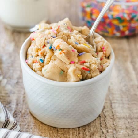 A small bowl of edible sugar cookie dough with sprinkles sitting on a wooden table.