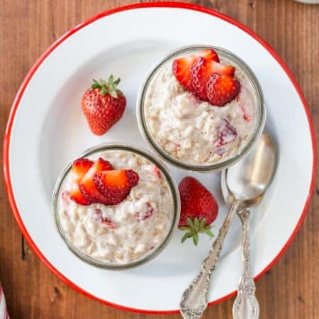 Two bowls of strawberries and cream oatmeal, topped with strawberries, sitting with two spoons.
