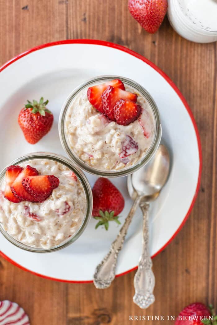 Two bowls of strawberries and cream oatmeal sitting with two spoons.
