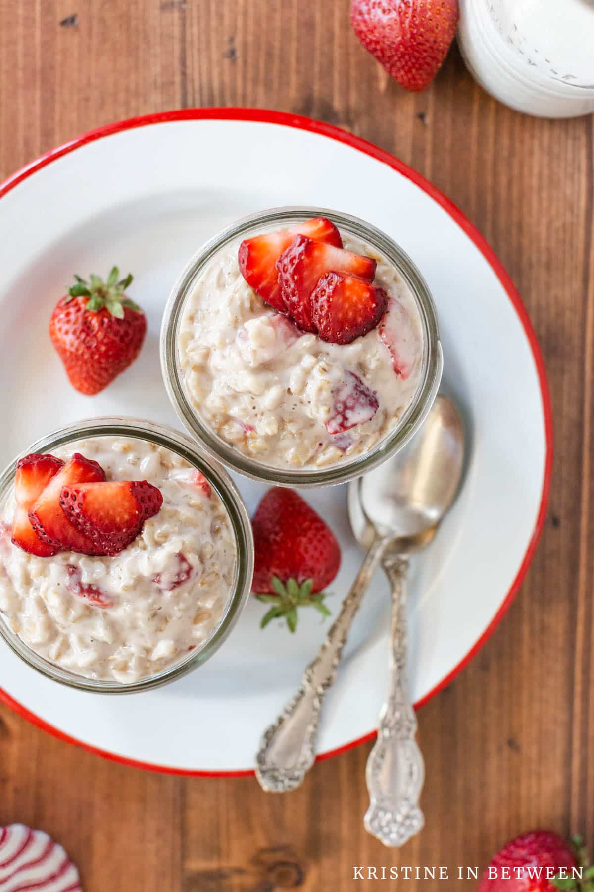Two bowls of strawberries and cream oatmeal sitting with two spoons.