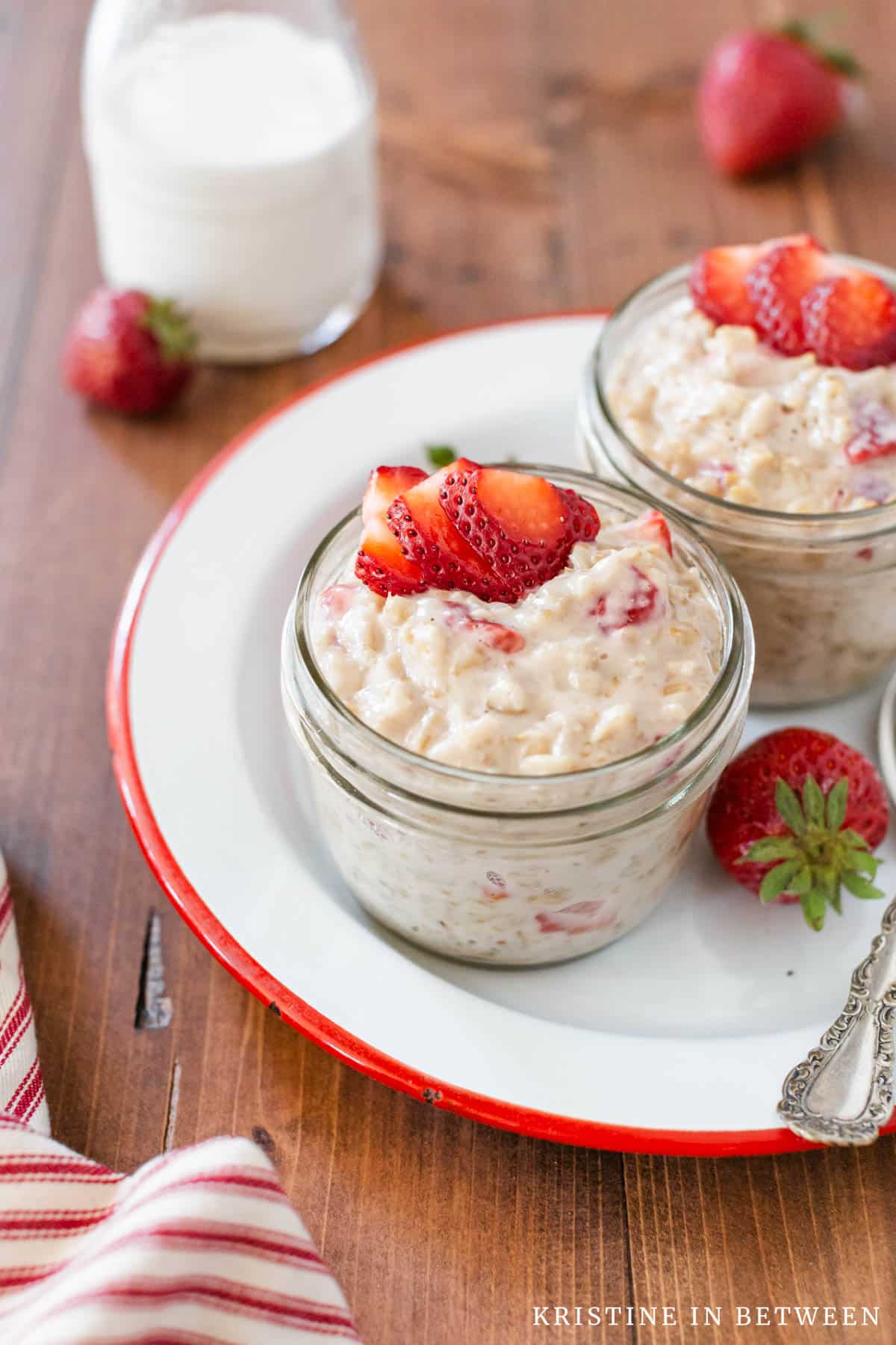 Strawberries and cream oatmeal in two jars with milk in the background.