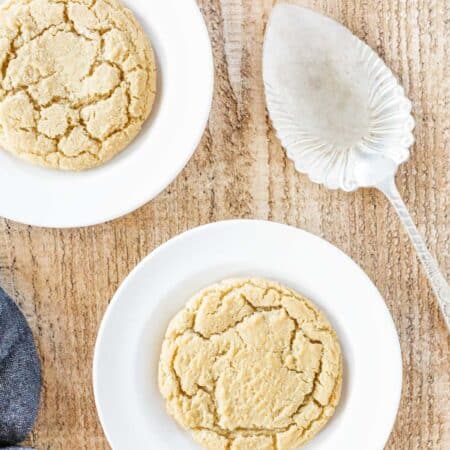 Two sugar cookies sitting on white plates with a spatula sitting next to them.
