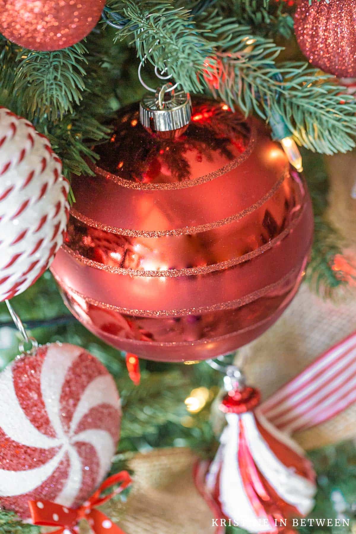 Red ornaments hanging on a Christmas tree with burlap ribbon.