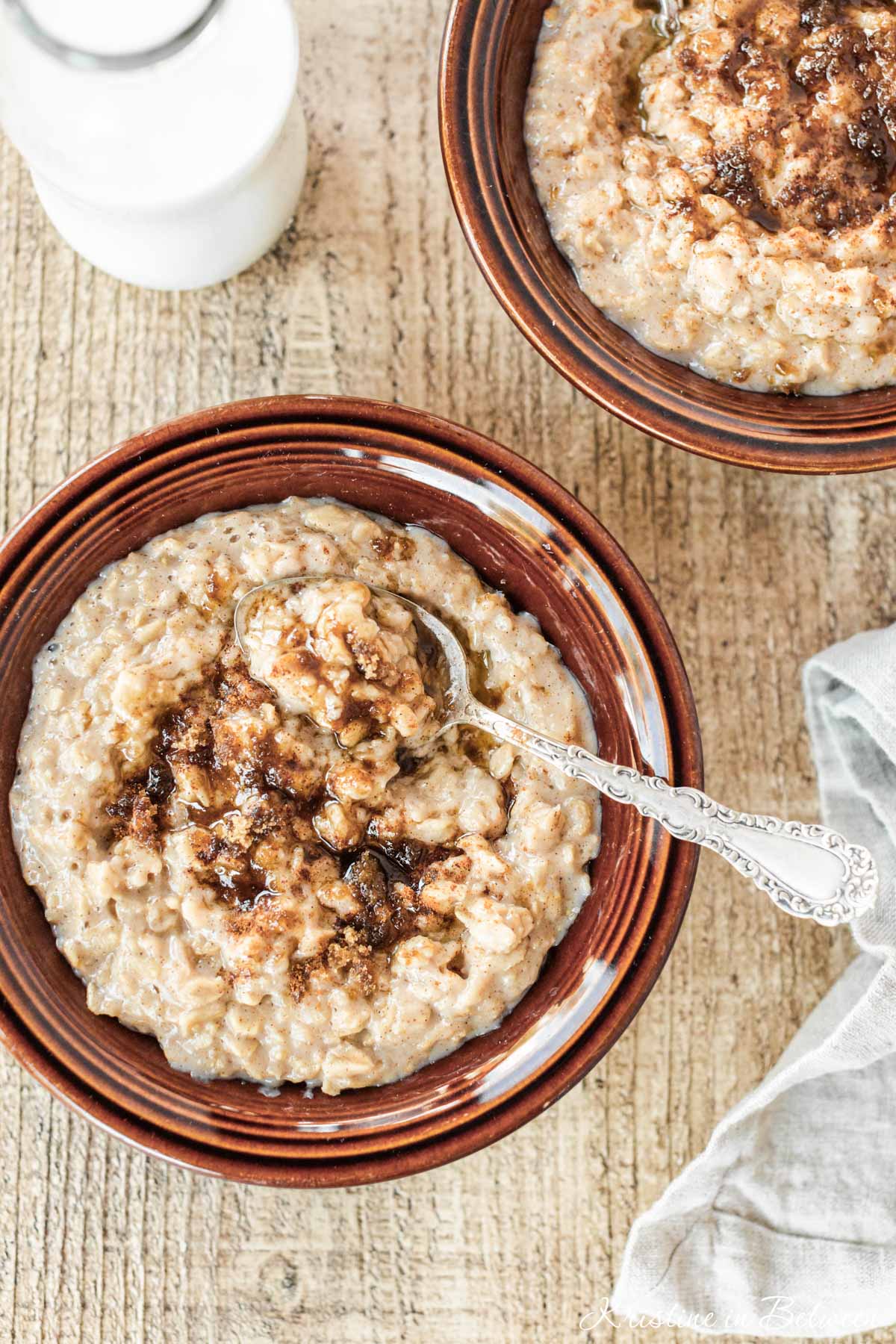 Two bowls of cooked oatmeal with spoons, topped with brown sugar and cinnamon.