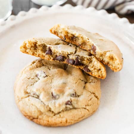Two chocolate chip cookies sitting on a white plate with one broken in half.