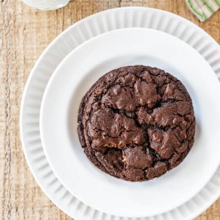 Two dark chocolate cookies stacked up on a white plate.
