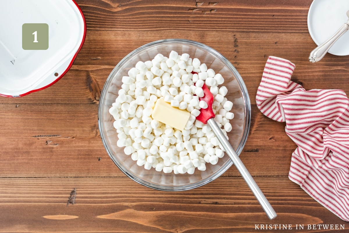 Mini marshmallows and butter in a glass bowl with a rubber spatula.