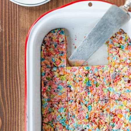 A pan of Fruity Pebbles Krispies Treats with an old spatula laying in the pan.