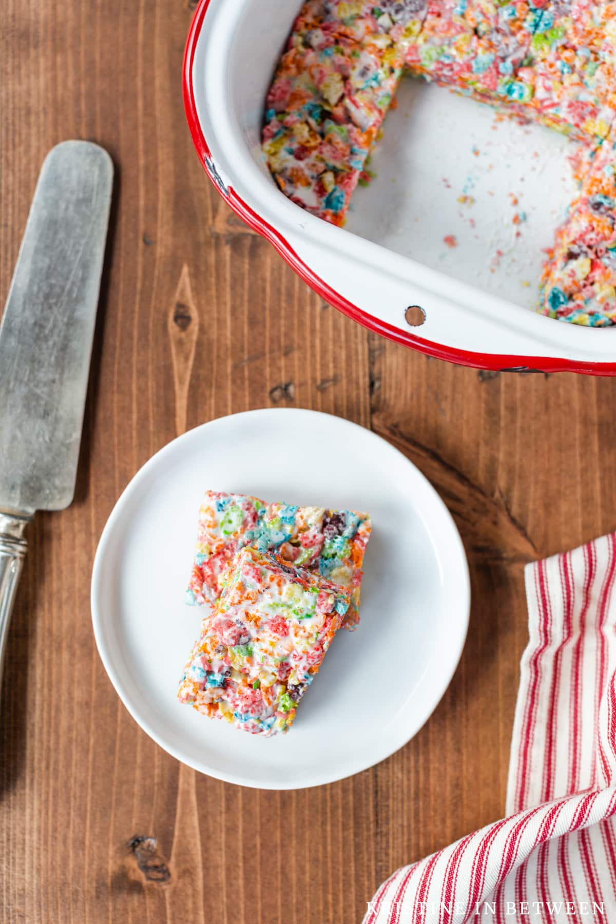 Fruity Pebbles Krispies Treats on a white plate with a spatula next to them.