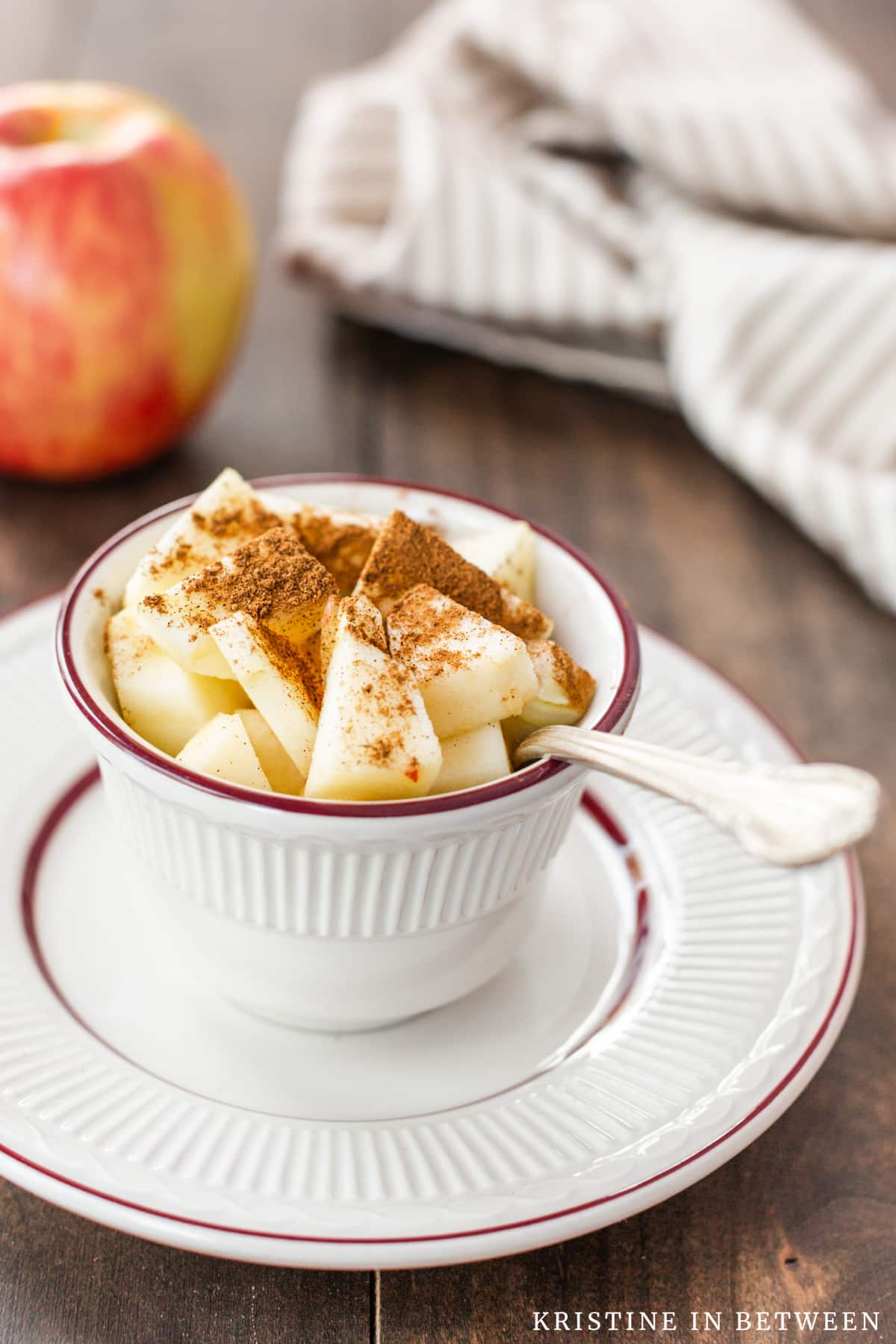 Chopped apples in a small bowl with apple pie spice sprinkled on top with an apple in the background.