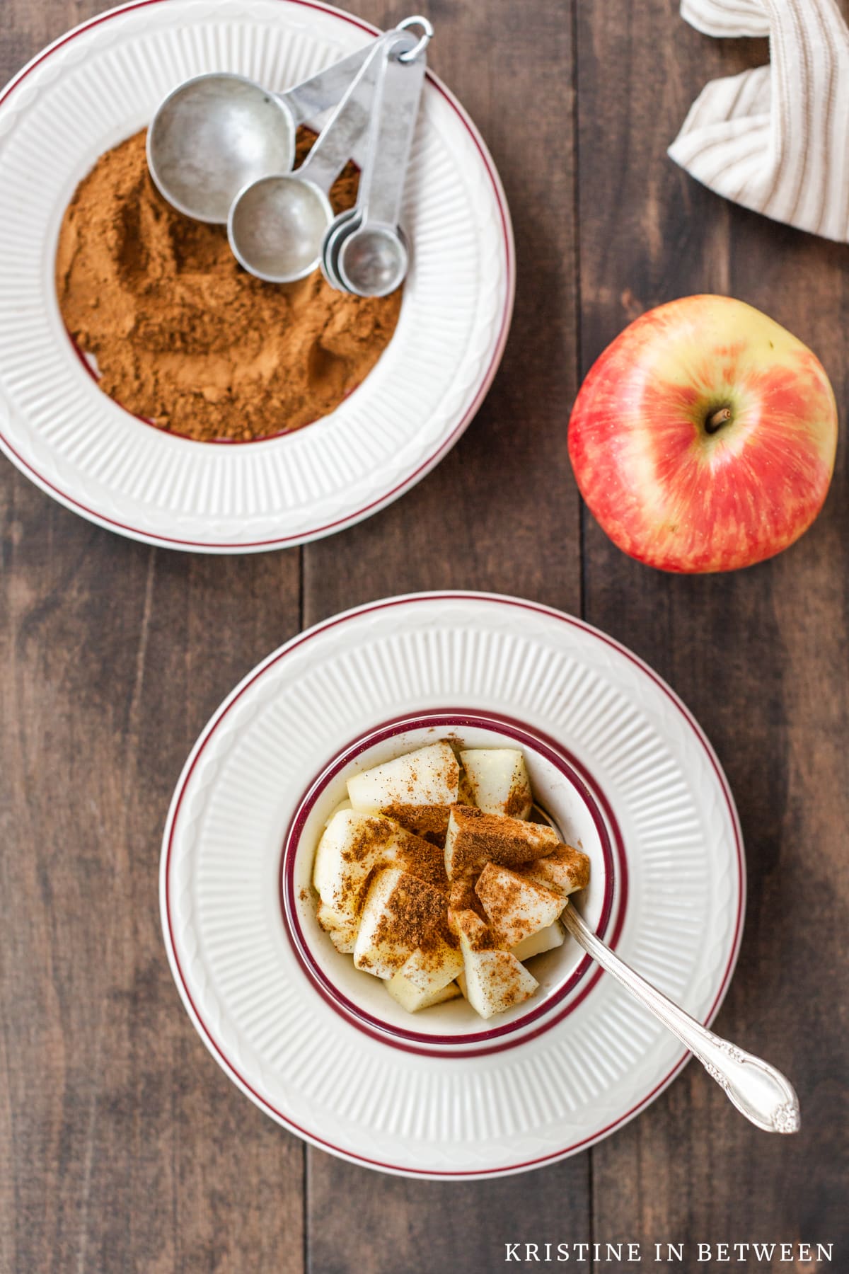 Chopped apples with apple pie spice sprinkled on top with a plate of apple pie spice in the background.
