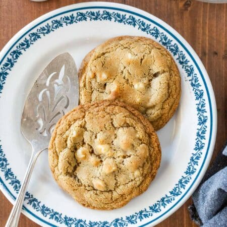 Two macadamia nut cookies sitting on a plate with a blue border and an antique spatula.