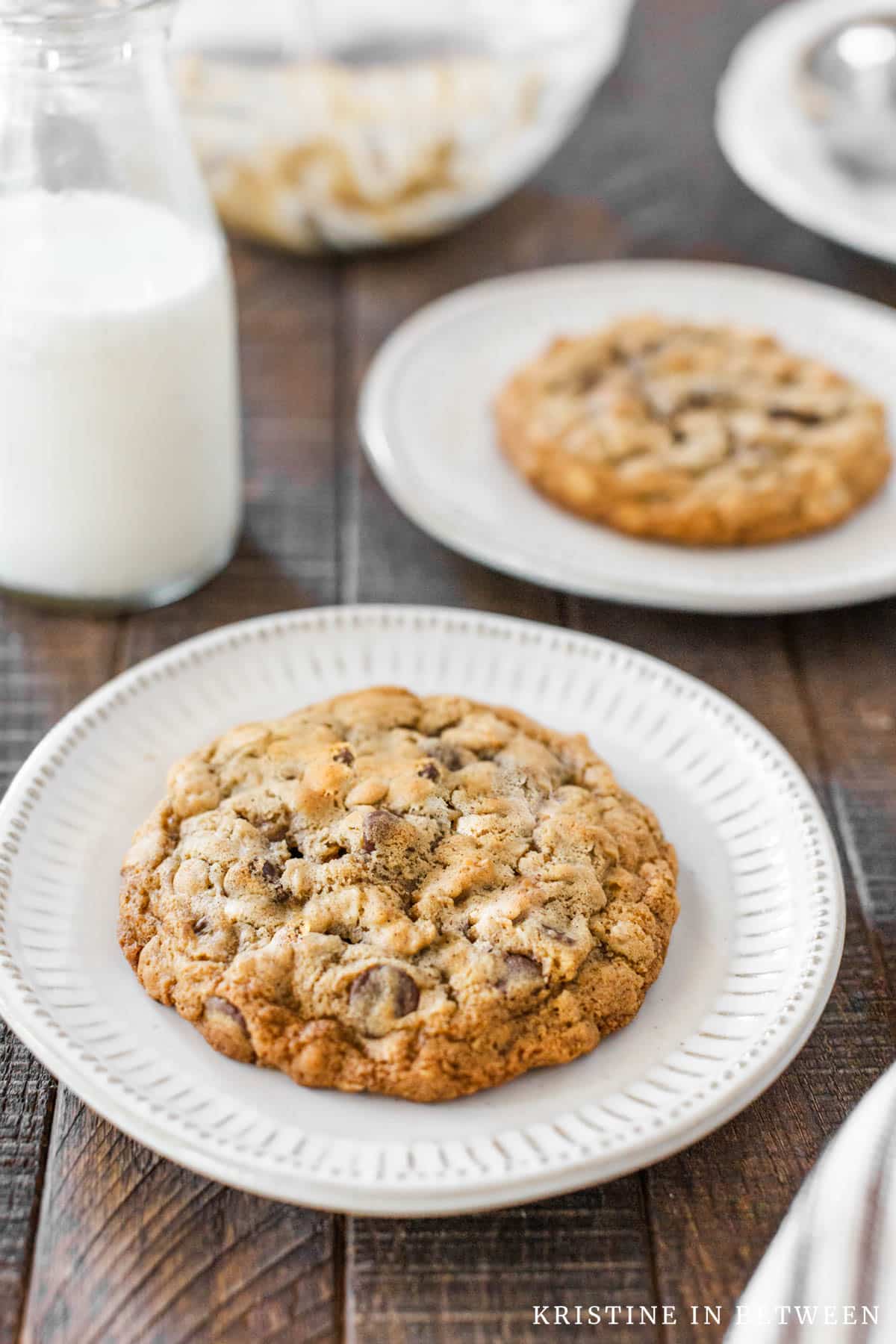 Oatmeal cookies sitting on small white plates with a jar of milk in the background.