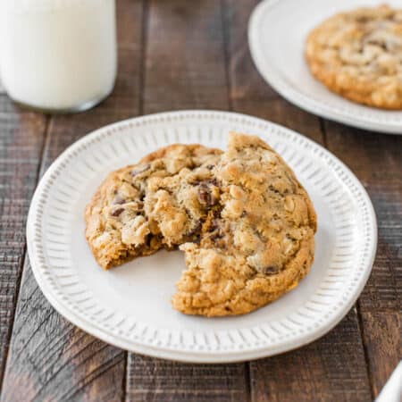 Two oatmeal cookies stacked upon white plates with a jar of milk in the background.