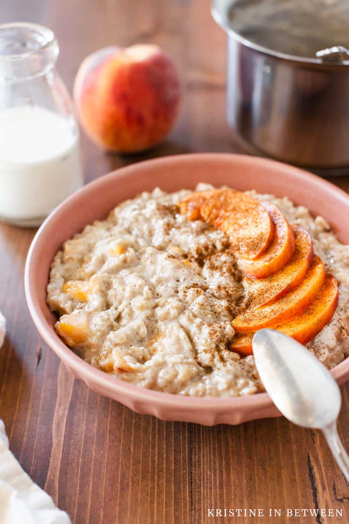 Oatmeal in a light pink bowl topped with sliced peaches and cinnamon.