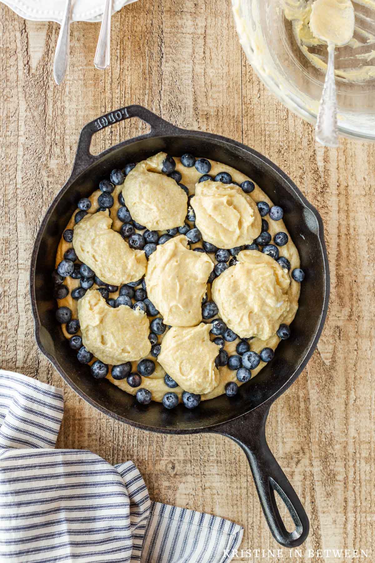 Cake batter dolloped on top of blueberries in a cast iron pan.