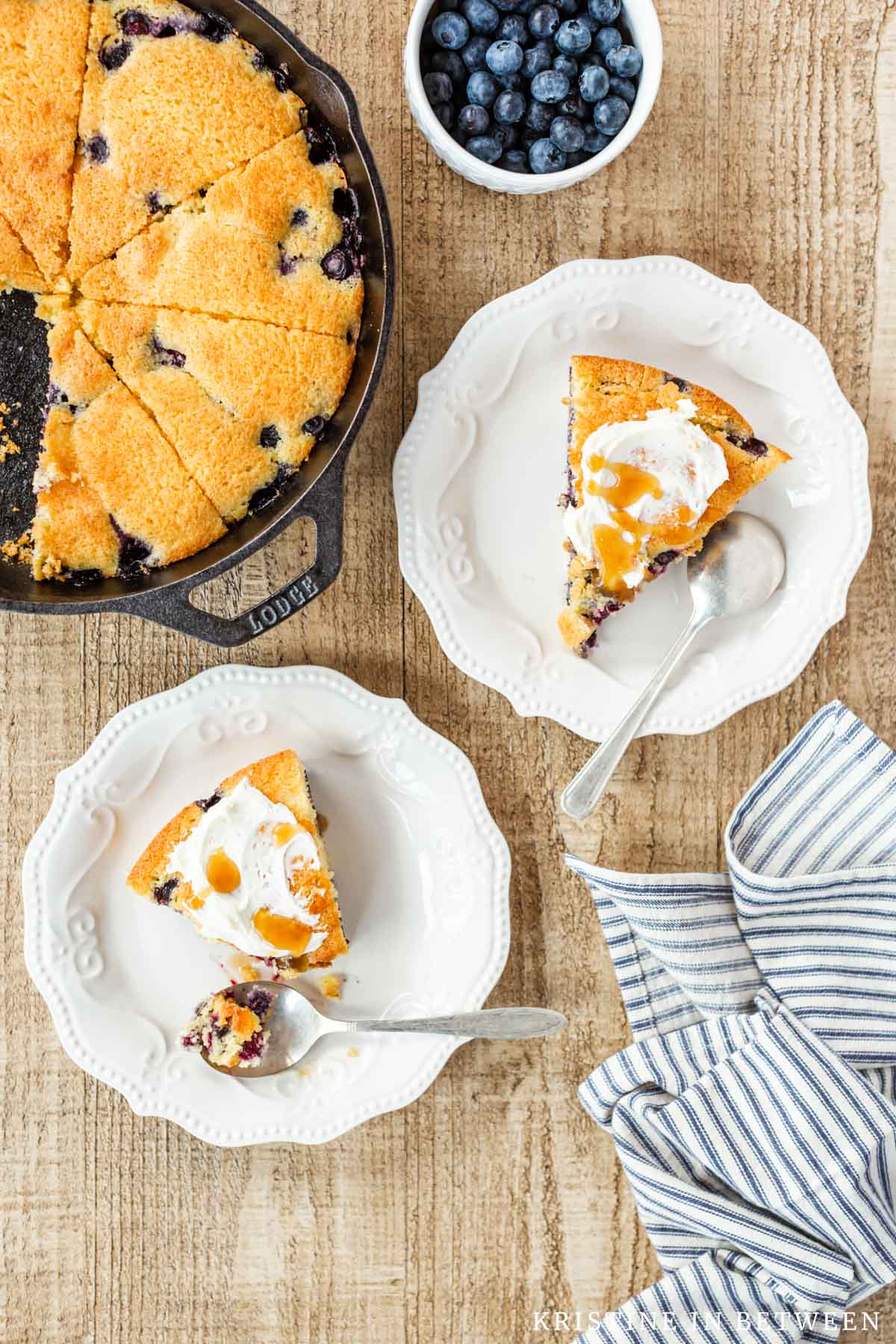 Two pieces of blueberry cornmeal skillet cake on white plates, drizzled with honey.