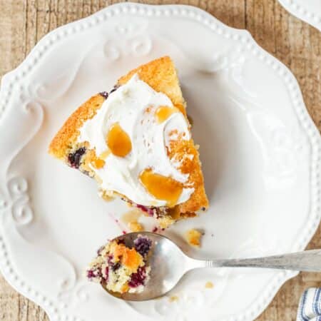 A slice of blueberry cornmeal skillet cake on a white plate with a spoon.