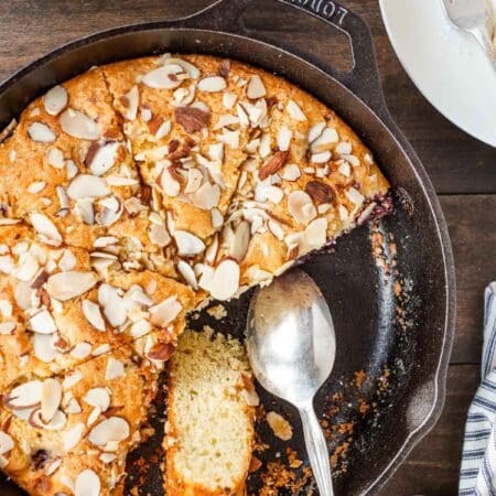 A cherry almond skillet cake in a cast iron skillet with a few slices missing.
