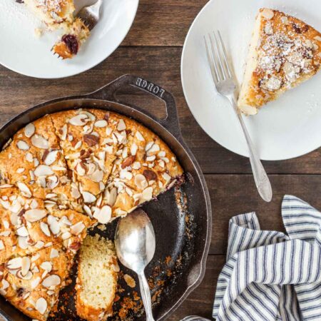 A cherry almond skillet cake sitting with two slices on white plates with forks.