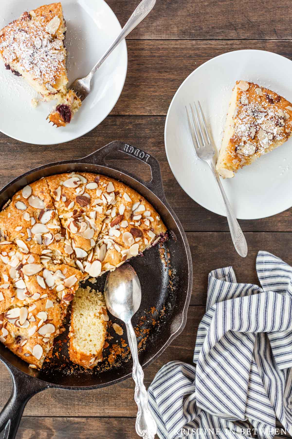 A cherry almond skillet cake sitting with two slices on white plates with forks.