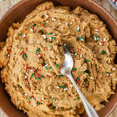 Edible gingerbread cookie dough in a brown bowl with a bite on a spoon on top.
