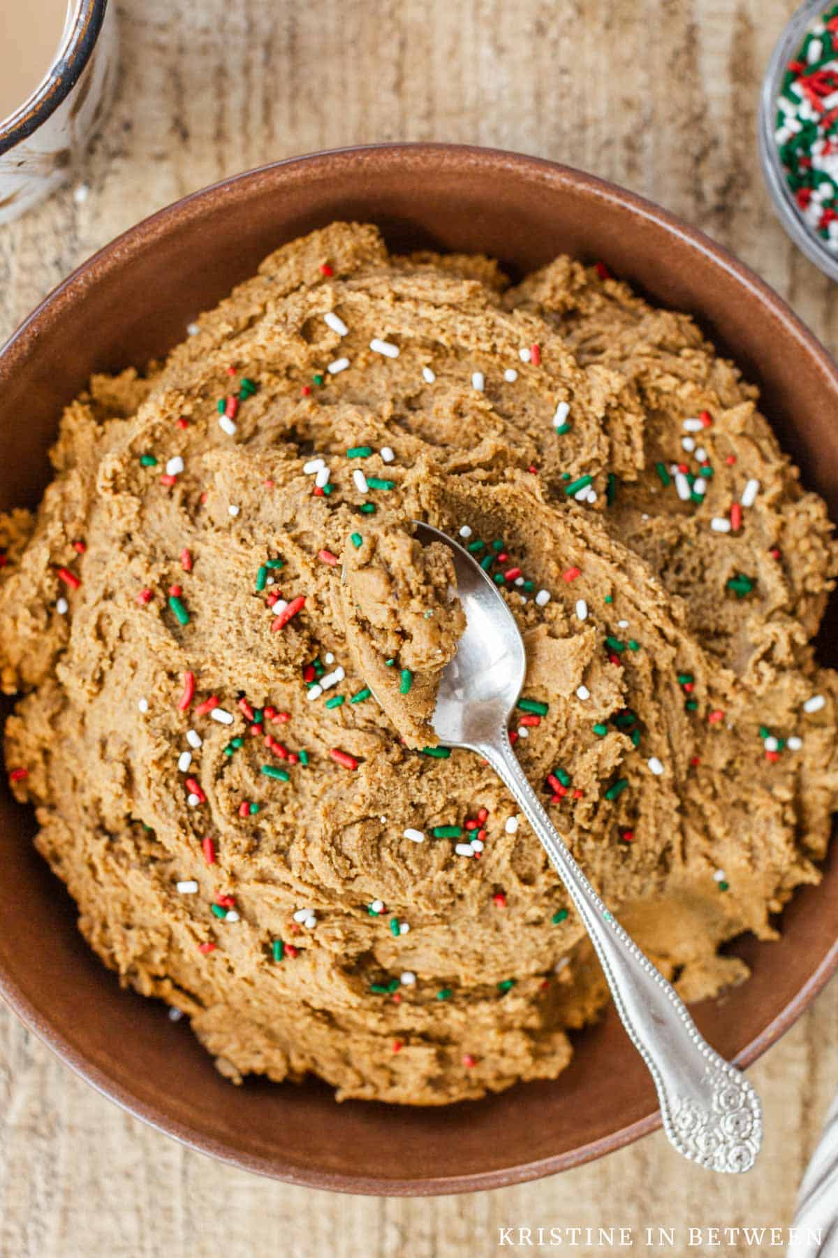 Edible gingerbread cookie dough in a brown bowl with a bite on a spoon on top.