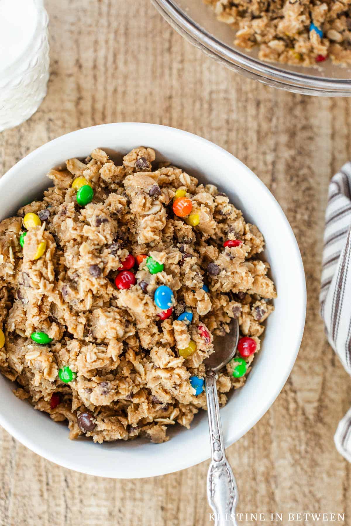 Edible cookie dough in a small white bowl with a spoon and a glass of milk in the background.