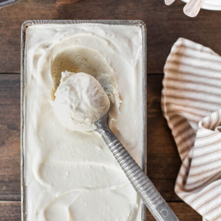 Vanilla no-churn ice cream in a loaf pan with a scoop on top.